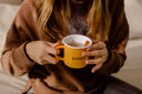 Deux mains autour d’un mug GIMBER fumant, avec un bâton de cannelle