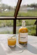 Une bouteille de GIMBER Original et un verre servi, sur une table au soleil