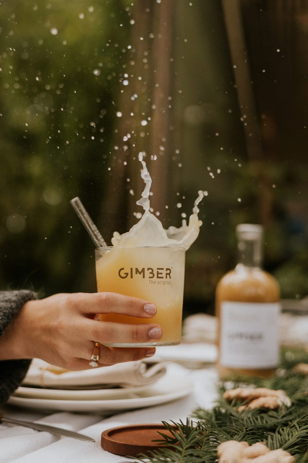 Un verre de GIMBER qui éclabousse, la bouteille posée à côté sur la table