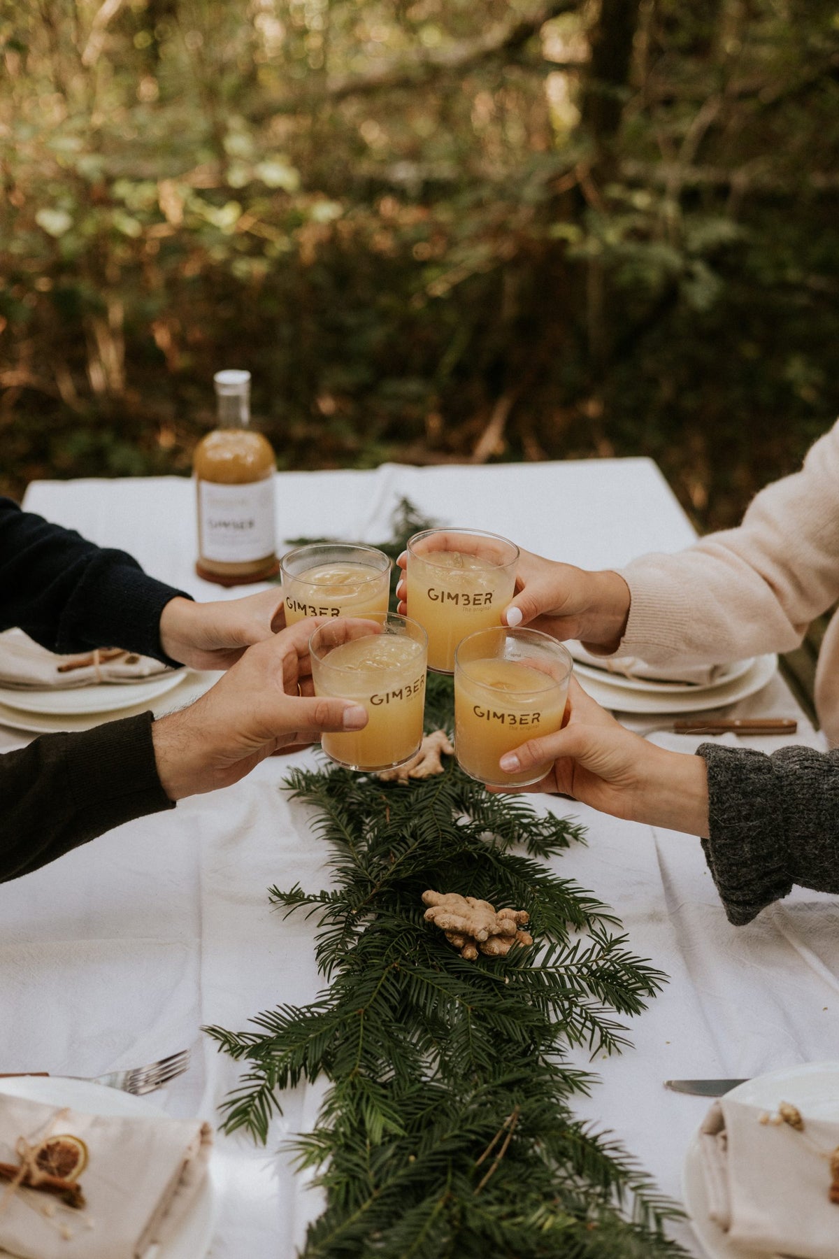 Quatre verres de GIMBER qui trinquent autour d'une table d'hiver, la bouteille en fond